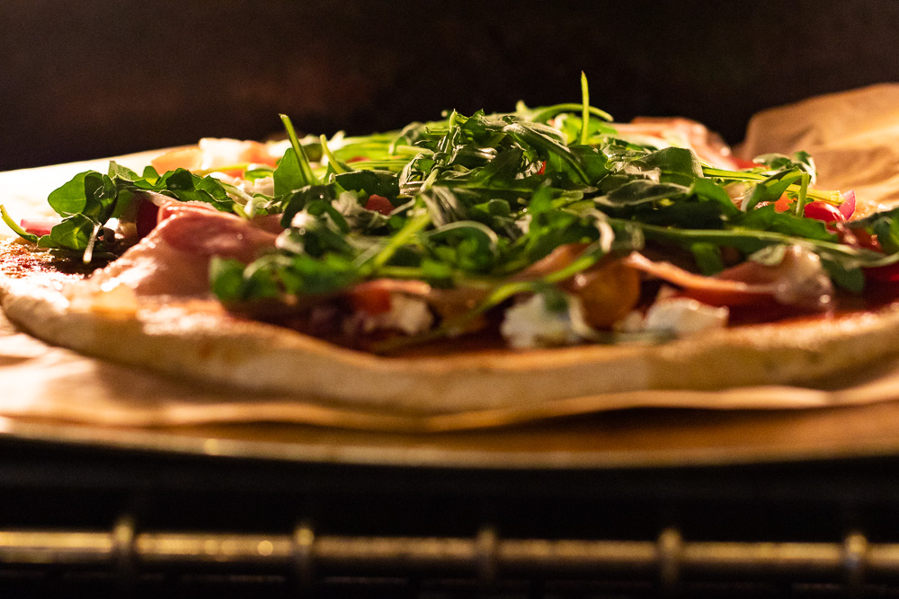 Gluten free prosciutto, arugula and cashew cheese pizza in oven