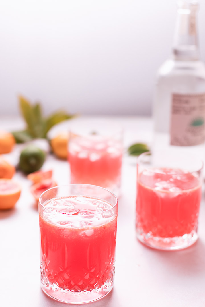 blood orange spritzer with tequila bottle and full and halved oranges.