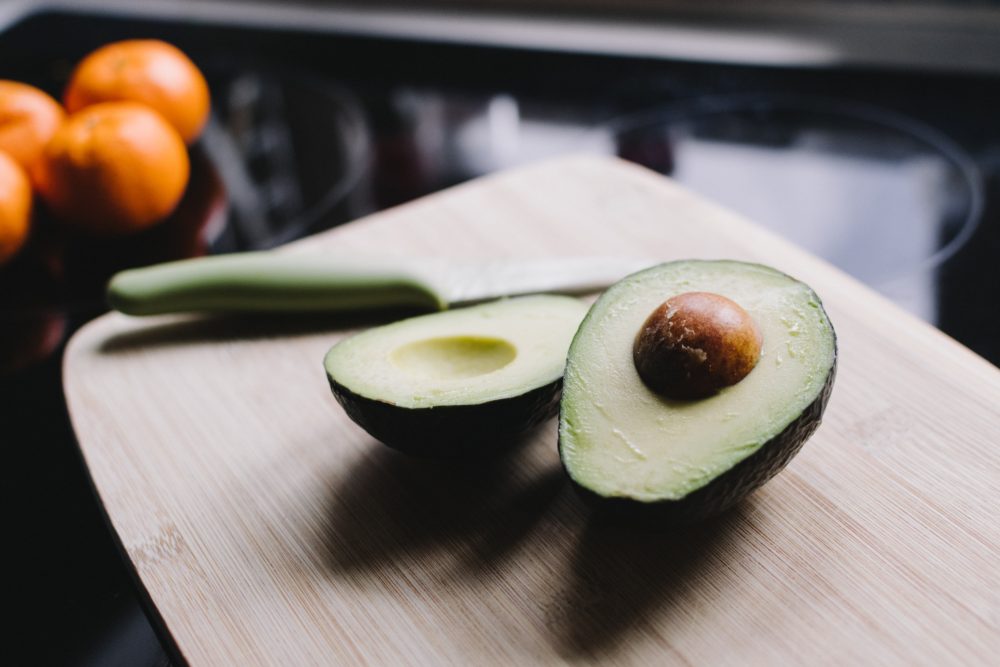 sliced avocado with knife on wooden board