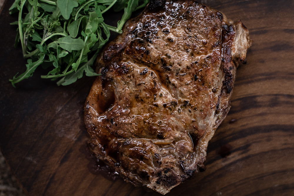 grilled steak with greens on wood board